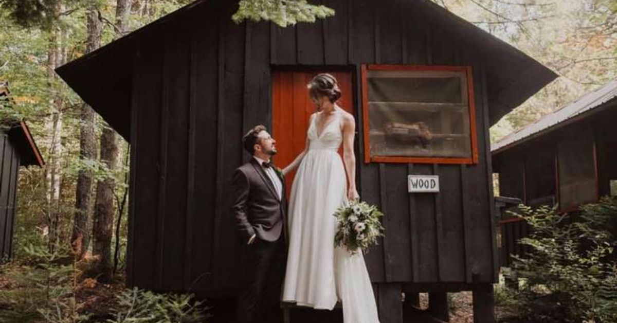 couple standing in front of a brown cabin with red door in wedding clothes