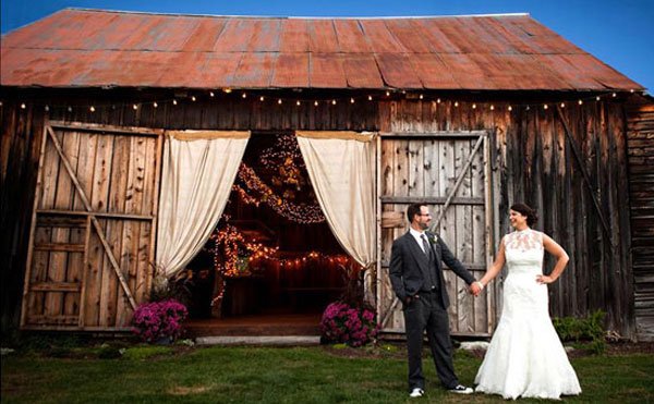 bride and room holding hands in front of a barn with curtains drawn